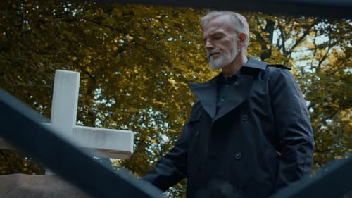 Mourning Man Standing beside Grave with Memorial Cross in Cemetery