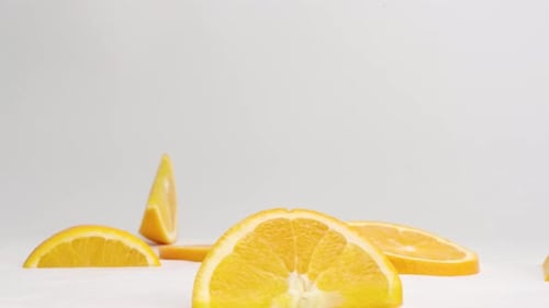 Bright orange citrus slices bouncing on white table top in slow motion