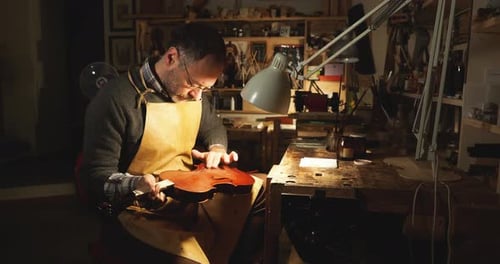 Luthier carefully applying varnish on a new handcrafted violin in his workshop in Cremona, Italy