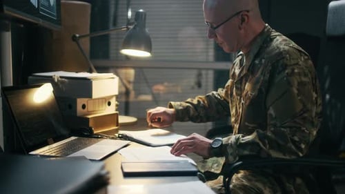 Adult Commander Filling Documents in front of Laptop in Military Office