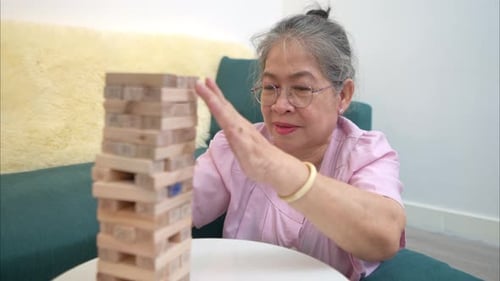 Senior Woman Plays Jenga Game at Home on Table