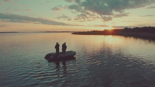 Friends fishing at sunset. Two amateur anglers fishing from the boat on a clam lake during sunset