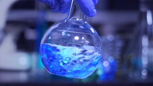 Chemical Research Mixing Glowing Blue and Green Fluorescent Liquid in a Flask