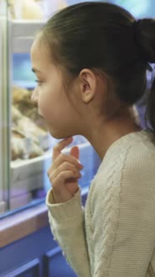 Thoughtful Little Girl Admiring Delicious Pastries at a Charming Bakery