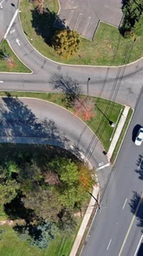 Traffic Intersection Surrounded By Greenery and Parking Lot Viewed From Above in Urban Setting