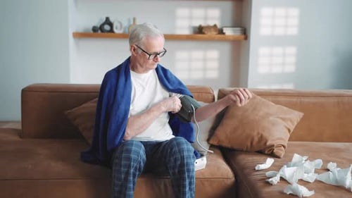 Senior Man Checks Blood Pressure on Sofa at Home