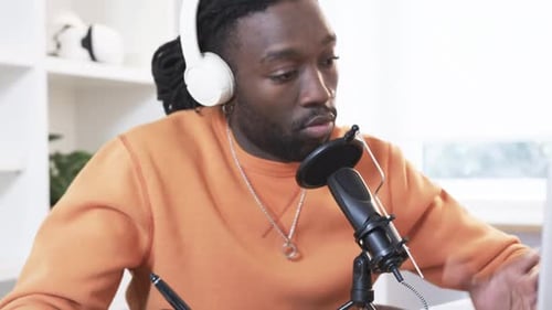 Homme afro-américain écrivant dans un carnet au bureau en enfilant des écouteurs et en parlant dans un microphone