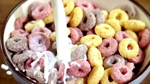 Milk Pouring Over Multi-Colored Cereal Loops in a Bowl