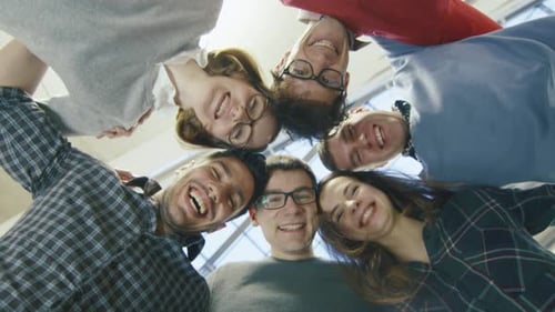 Multi-ethnic group of happy young students are standing in a circle and looking down at the camera.