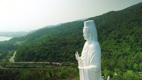 Peaceful White Buddha Statue Gazing Over Verdant Coastal Landscape Sandy Shoreline and Urban Skyline