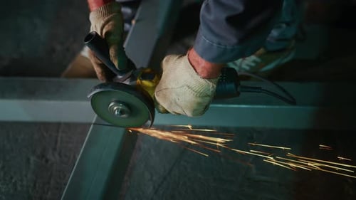 Metal worker cutting steel with grinder, sparks flying