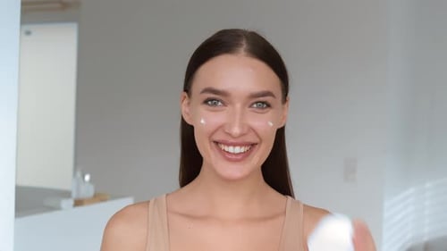 Sourire éclatant d'une femme appliquant des soins de la peau dans une pièce lumineuse
