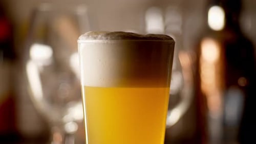 Close up of craft Beer being poured in to a pint glass to top it off, light background