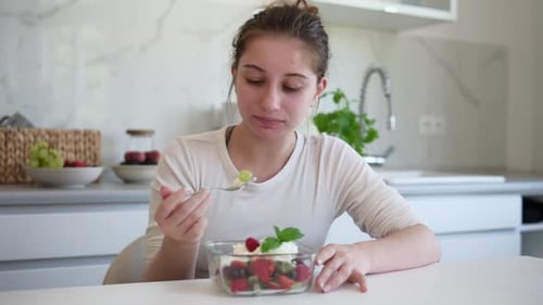 Woman Eating Fresh Fruit Salad in Bright Kitchen