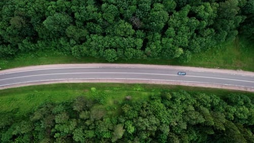 Aerial view from a drone flying over a scenic road in a verdant deciduous forest.