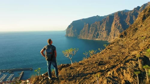Backpacker Man Stands on Edge of Sheer Cliff with Ocean View