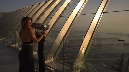 A Woman is Seen Standing on Top of a Tall Building Overlooking the UAE Dubai Sunset at the Palm