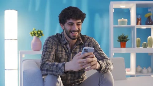 Smiling Young Adult Using Phone on Gray Couch