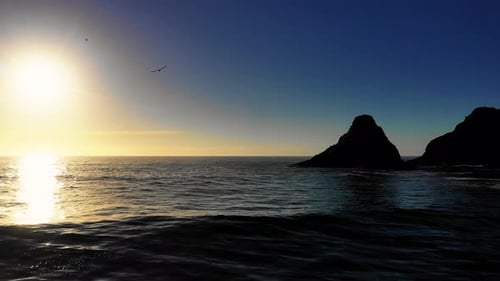 Birds flying over the waves and dark blue ocean water at sunset with large silhouetted rock cliffs i
