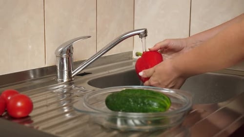 01 1Washing peppers and cucumbers under running water. Preparing vegetable dishes.