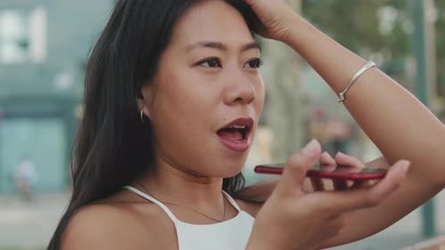 Close up, young woman sitting on bench sends voice message with mobile phone