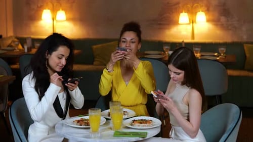 Smiling Pretty Ladies Sitting in the Restaurant While Holding Smartphones and Making Photos of Food