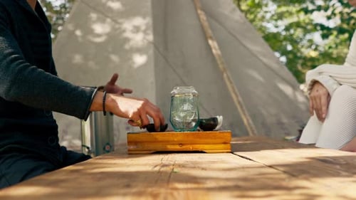The hands of a professional tea master who pours fresh natural green tea from a glass teapot into