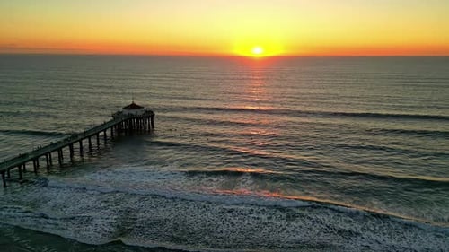 Aerial view of pier and waves during ocean sunrise near Manhattan Beach, California
