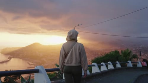 Girl in Hood Walking, Amazing Cloudy Sunset over City in the Background