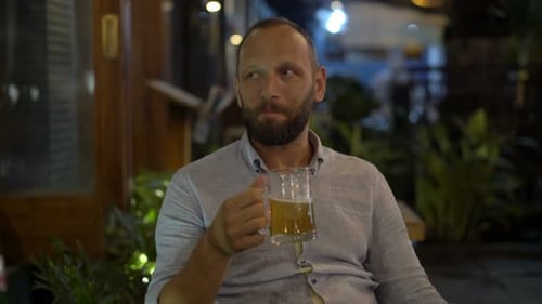 Handsome caucasian man enjoys refreshing beer at a cafe on a late night in the city