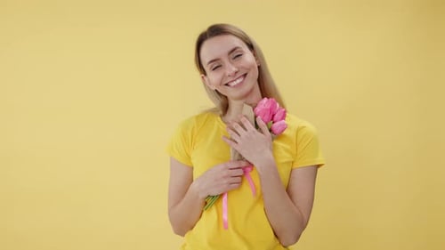 Mulher feliz segurando buquê de flores e sorrindo no estúdio com fundo amarelo