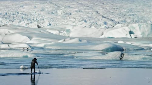 Solitary Person Standing on Glacier Lake Ice Watching Distant Icebergs