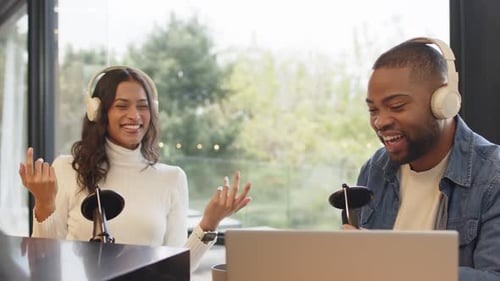 Diverse podcast hosts reacting to music cue, gesturing and adjusting headphones at desk for fun