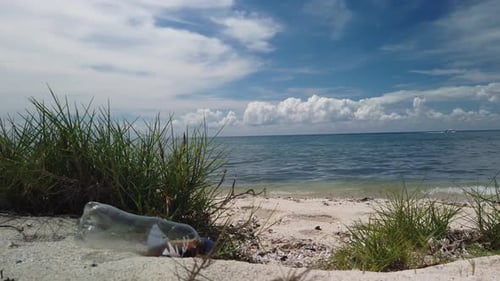White sand, bright blue sky and turquoise ocean with discarded plastic drink bottle. Ocean pollution
