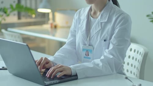 Young Asian Female Doctor Working on Laptop at Desk in Clinic