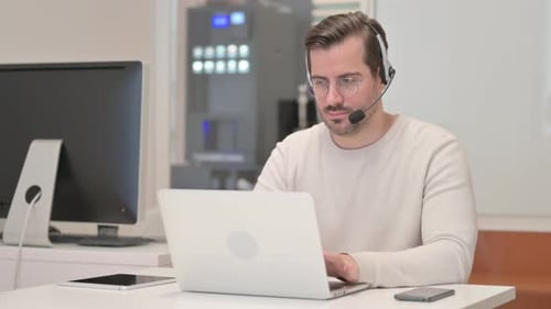 Young Man with Headset Working on Laptop in Call Center