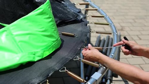 Homem monta um novo trampolim do lado de fora e estica sua tela com molas