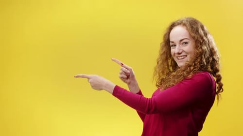 Portrait of Young Woman in a Studio on Yellow Background Pointing Fingers