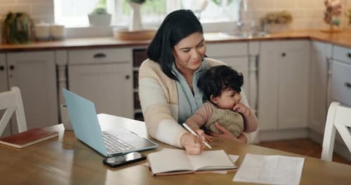 Mother Holding Baby Writing at Table with Laptop