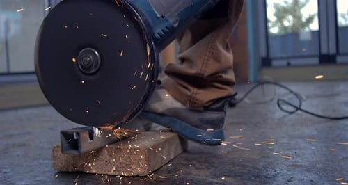 Worker using grinder on metal in workshop, sparks shooting off in slow motion, controlled and