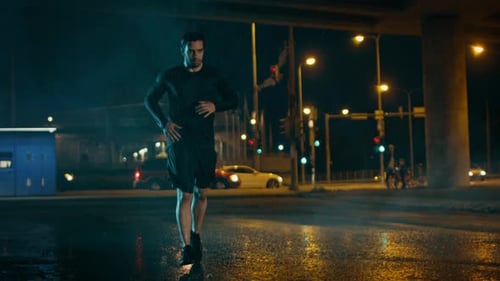 Athletic Muscular Young Man in Sports Outfit is Jogging in the Street on a Rainy Evening. He is Run