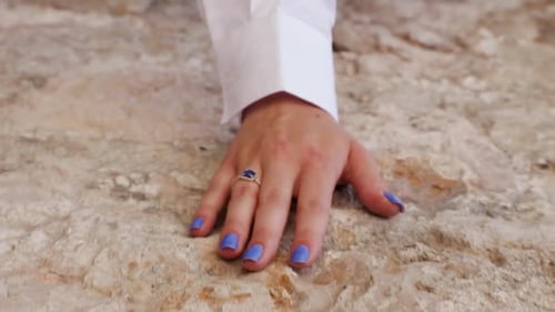 Young girl wearing a white long-sleeve shirt with a blue ring and blue nails runs her hand gently al