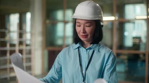 Asian Chinese Woman Engineer in Protective Helmet Checking Building Plan Paper Blueprint