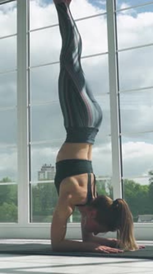Une jeune femme debout fait du yoga dans une pièce blanche remplie de lumière, la femme fait du yoga