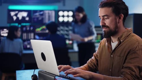 Man Typing on Laptop, Team Discussing in Modern Office
