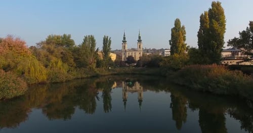 Establishing shot of a chatolic church in a park, reflection on the water and traffic in distance