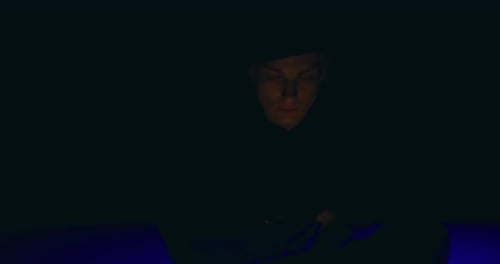 Hooded Figure Using Cell Phone in Dark
