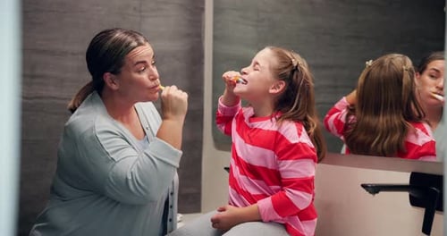 Mother and Daughter Brushing Teeth Together in Bathroom