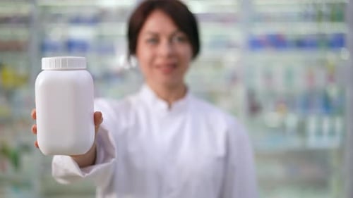 Closeup White Pill Bottle in Hand of Blurred Woman Standing in Pharmacy