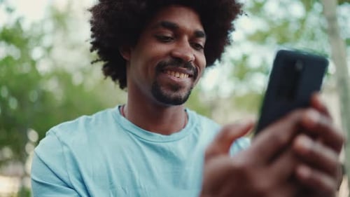 portrait of man sitting on city park bench and using his smartphone